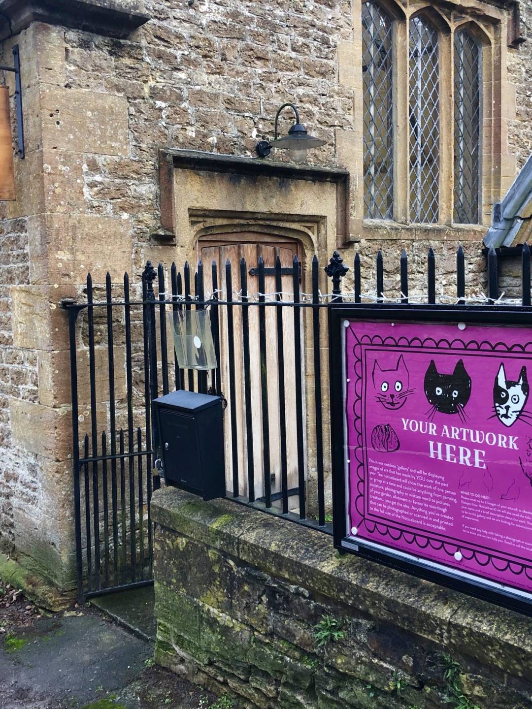 Noticeboard attached to the railings of OSR Projects. Inside the noticeboard is a pink lare poster with sketches and wording your artwork here.