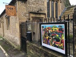 Noticeboard on railings outside of OSR Projects displaying colourful painting by Chris Burr
