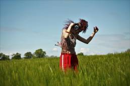 lady dancing in long grass, wearing headphones. Blue sky