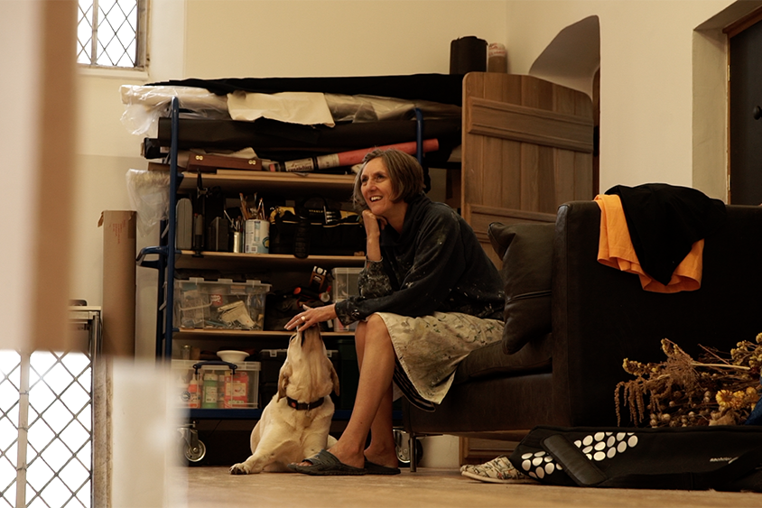 Anglea sitting on a sofa looking thoughtful with Flynn the guide dog lying at her feet