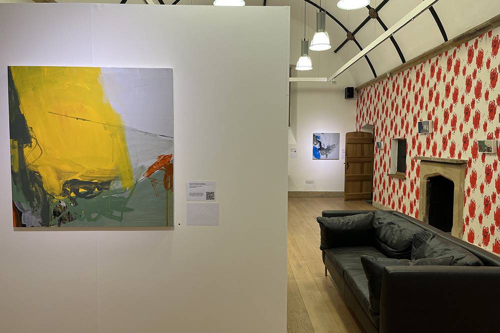 inside the gallery, with a yellow painting up close. Black sofa infront of the wall of hand printed wall paper