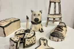 handbuilt white and outlined in black, paint brush, cake and slice, trainer, dog, lego brick and easel