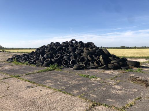 a huge pile of old tyres on a concrete surface on the edge of a field with blue sky