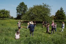 11 people staning in a grassey field, closet person wearing a huge straw sun hat