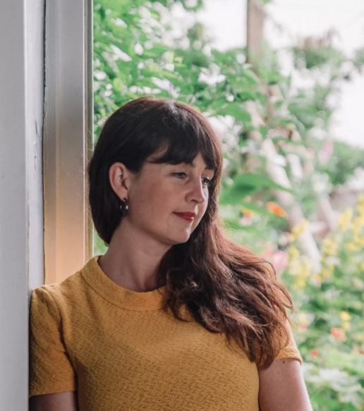 liv with long brown hair, looking right. She is wearing a yellow top
