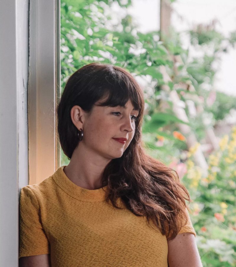 liv with long brown hair, looking right. She is wearing a yellow top